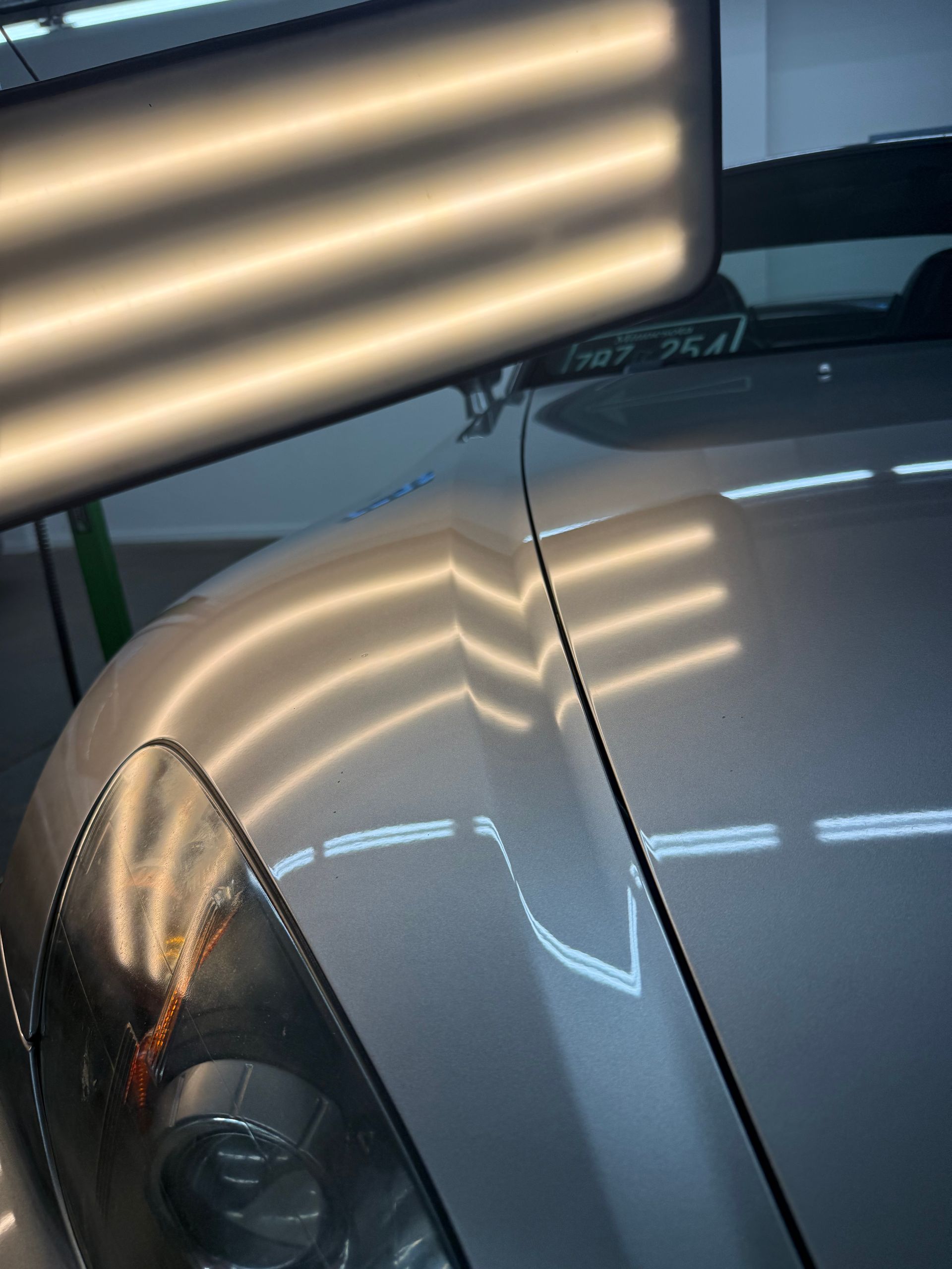 A bright LED work light reflects on a silver car fender, highlighting a dent repair using Paintless Dent Repair (PDR) lines.