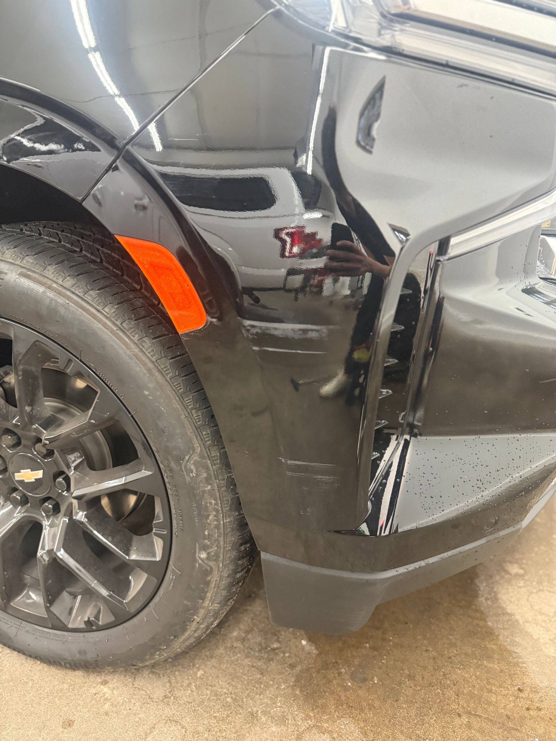 A close-up of a black car's front bumper, wheel, and orange side marker light.