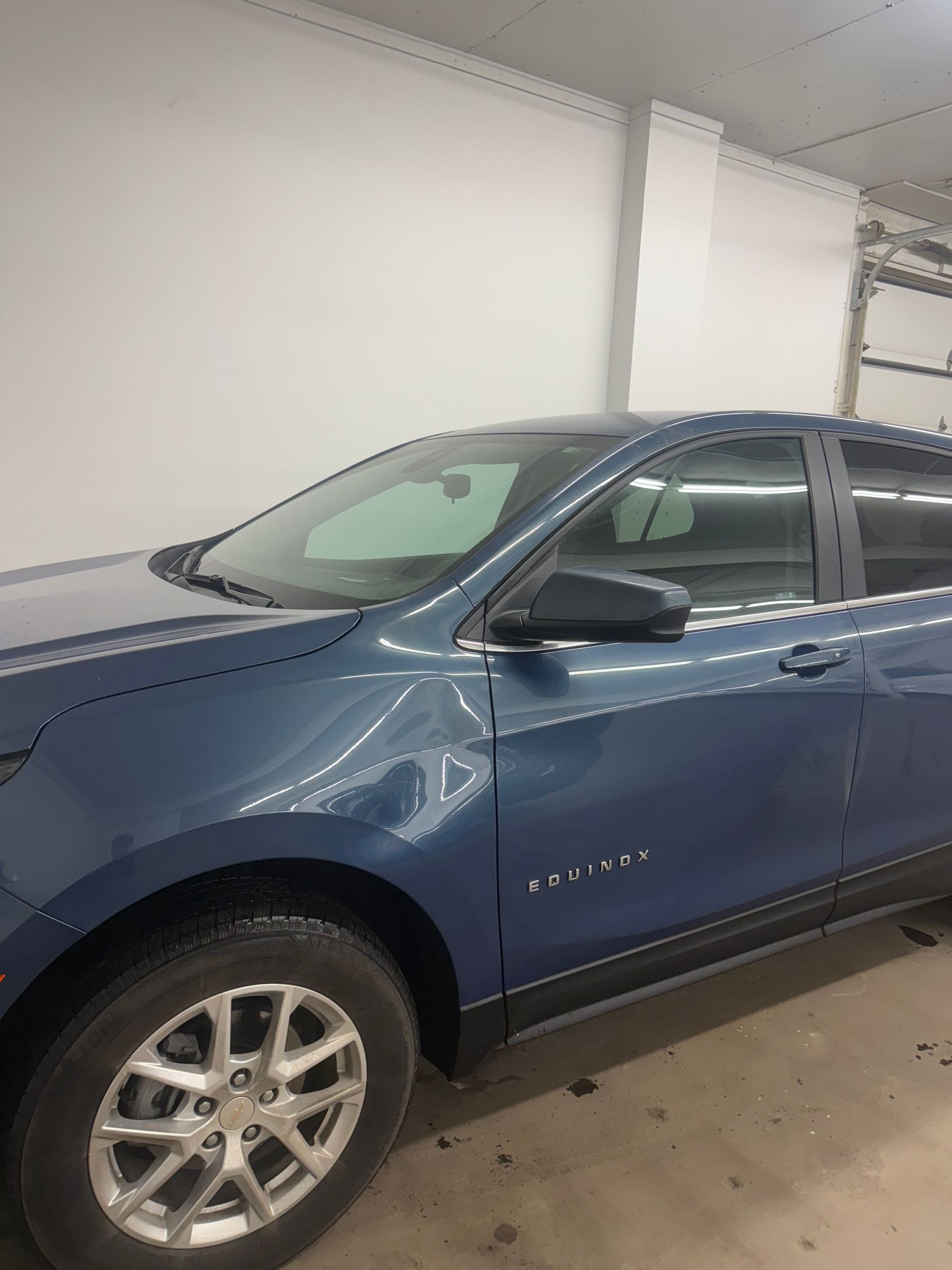A blue Chevrolet Equinox SUV parked indoors, showing the front passenger side, wheel, and door.