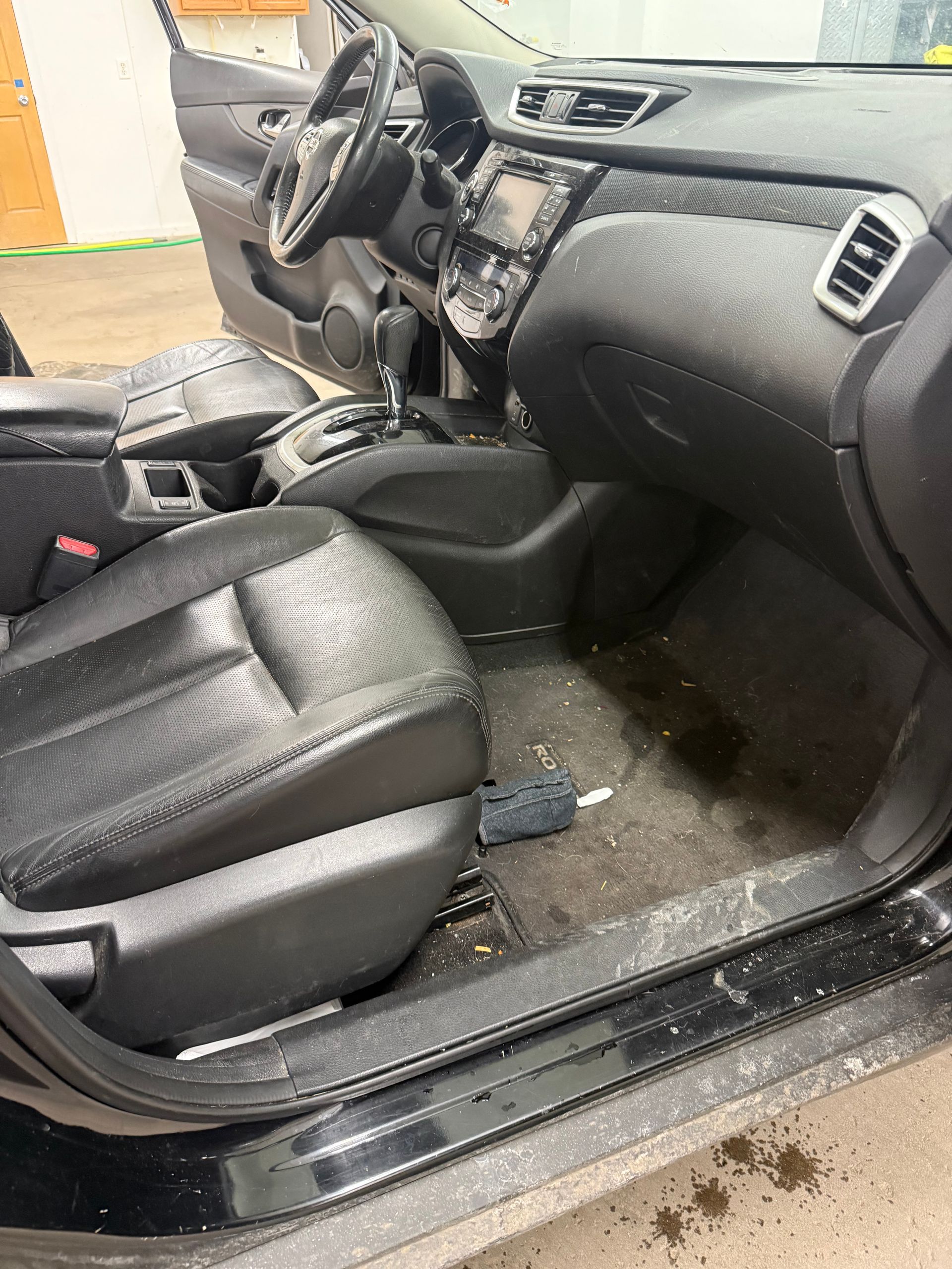 Interior of a car with a black leather passenger seat, dark dashboard, and dirty floor mat.