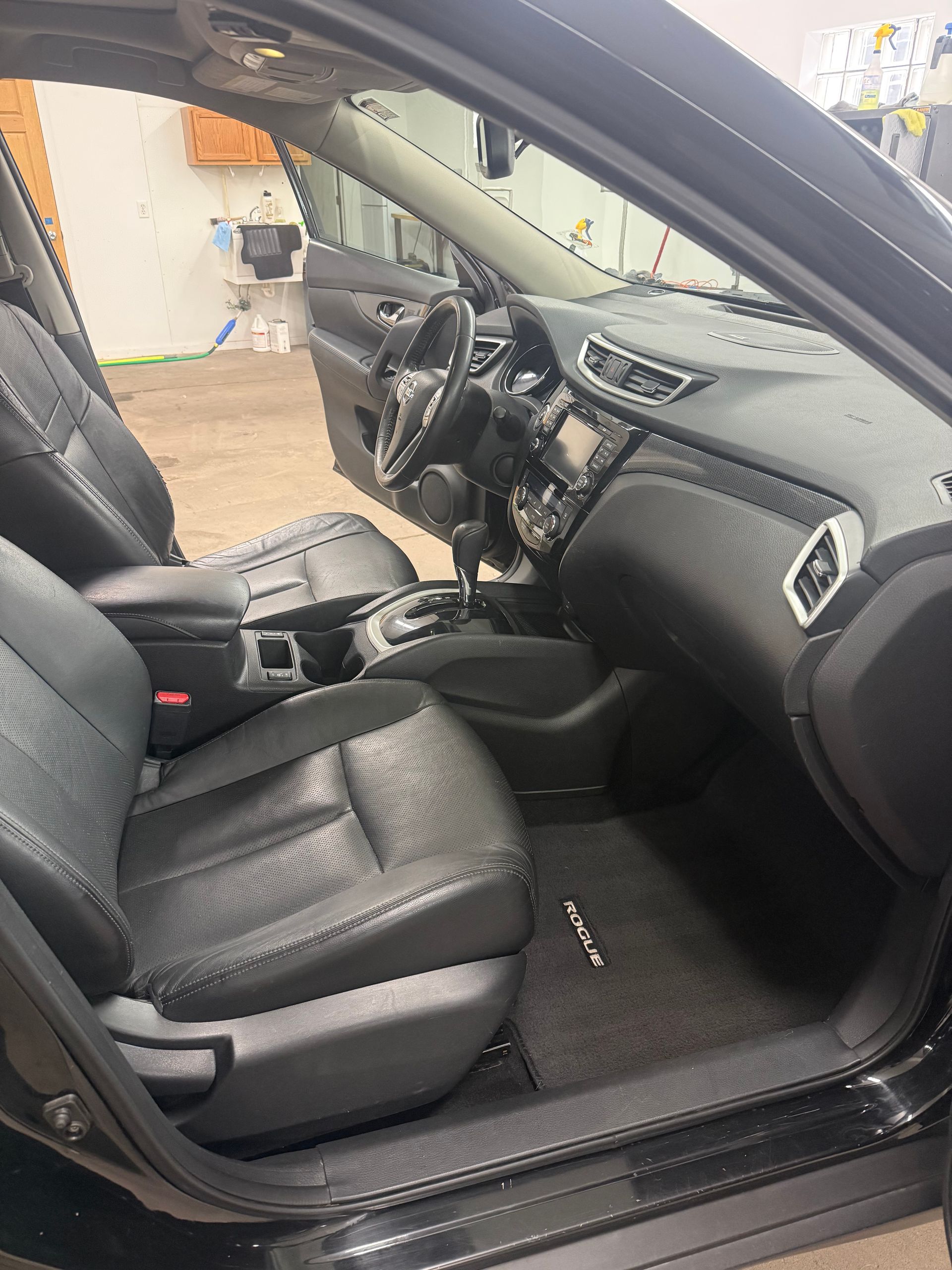 Black car interior showing front seats, dashboard, and steering wheel, viewed from the open driver-side door.