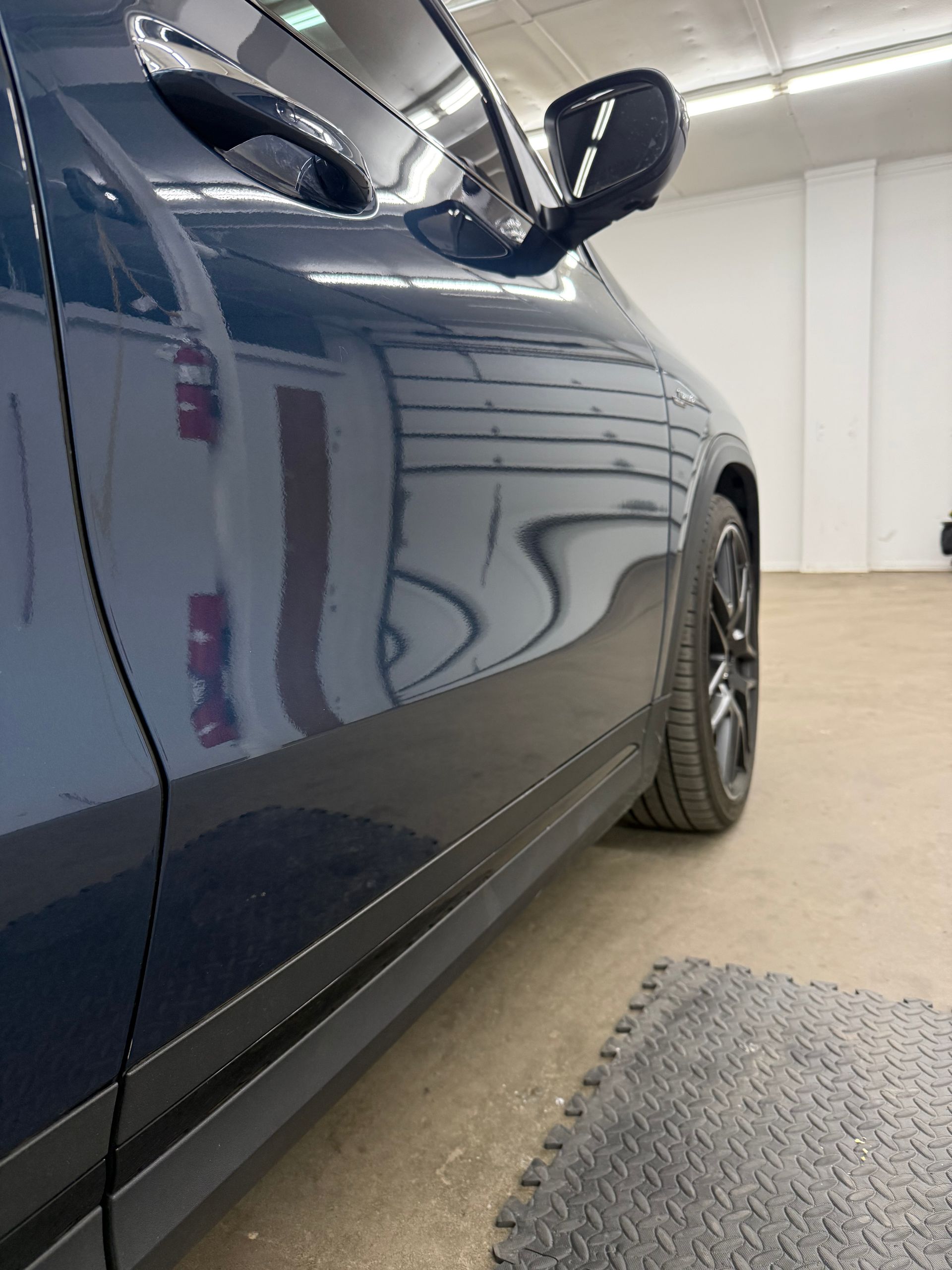 Close-up, low-angle view of the side of a shiny, dark blue car parked in a garage with a concrete floor.