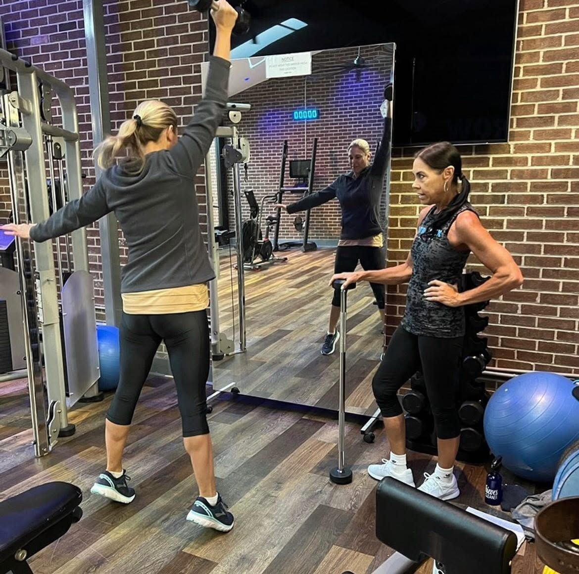 Two people exercising in a gym with mirrors, resistance bars, and a blue stability ball