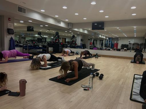 People exercising on mats in a mirrored gym studio, doing floor workouts with weights nearby