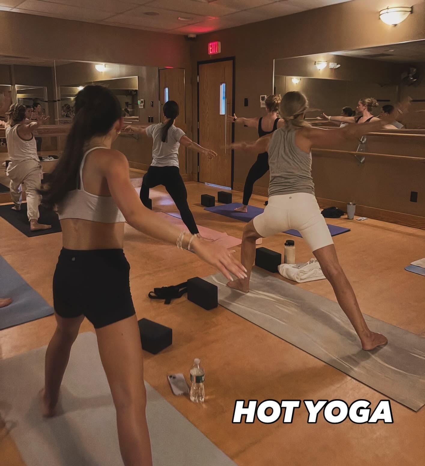 People doing hot yoga in a mirrored studio on mats, with warm lighting and “HOT YOGA” text.