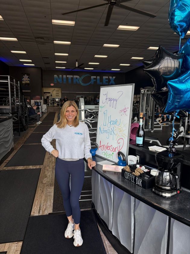 Woman standing in a gym lobby beside a promo sign and workout equipment