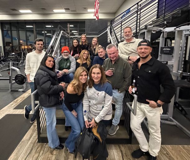 Group of people posing in a gym with weight racks and exercise equipment in the background.