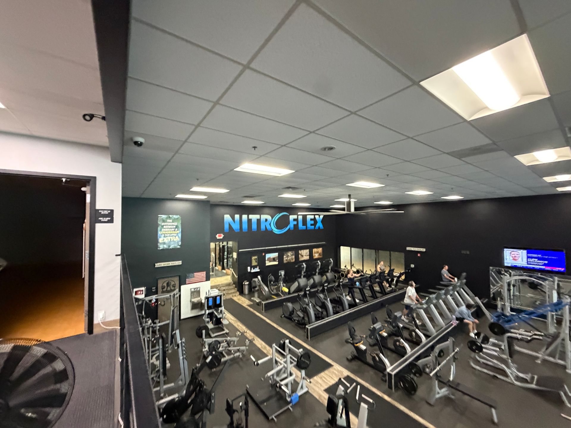 Spacious gym with rows of cardio machines, weight equipment, and a bright NITROFLEX sign on the wall