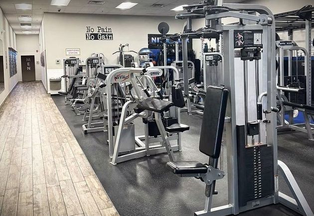 Empty gym interior with exercise machines and a wood floor corridor