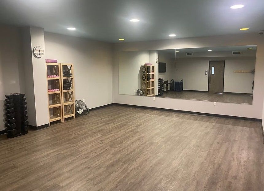 Empty fitness studio with wood floors, mirrors, ceiling lights, and racks of exercise equipment