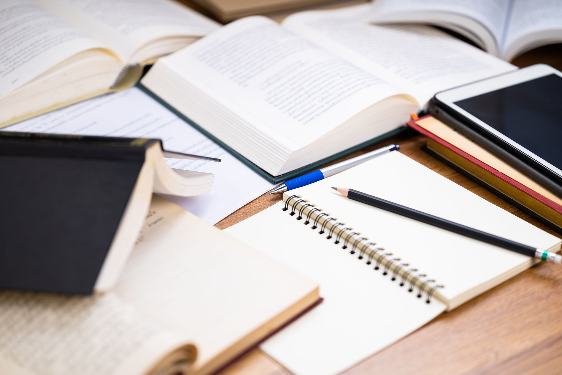 Open books, notebooks, and pens spread across a wooden desk for studying