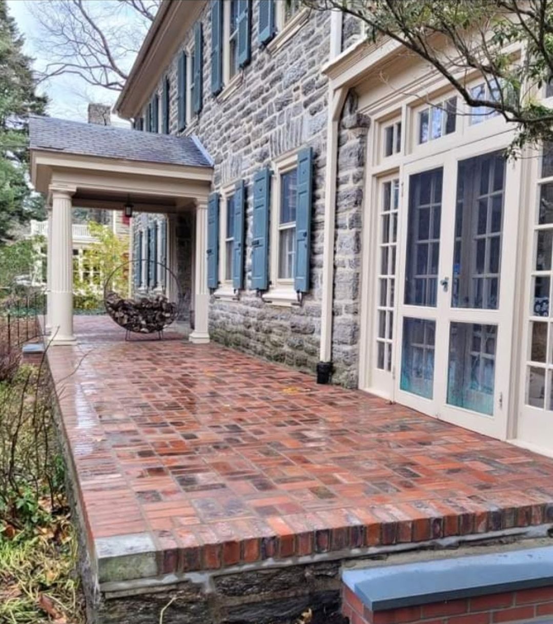 Stone house with brick patio and teal shutters.