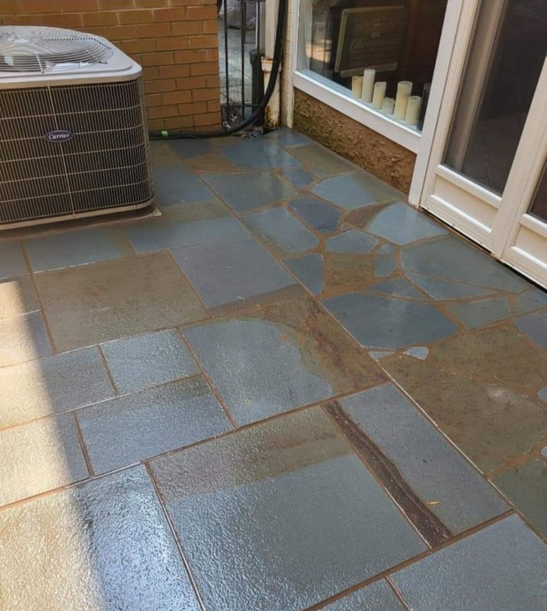 Wet blue and brown stone patio, next to an air conditioning unit and white door.
