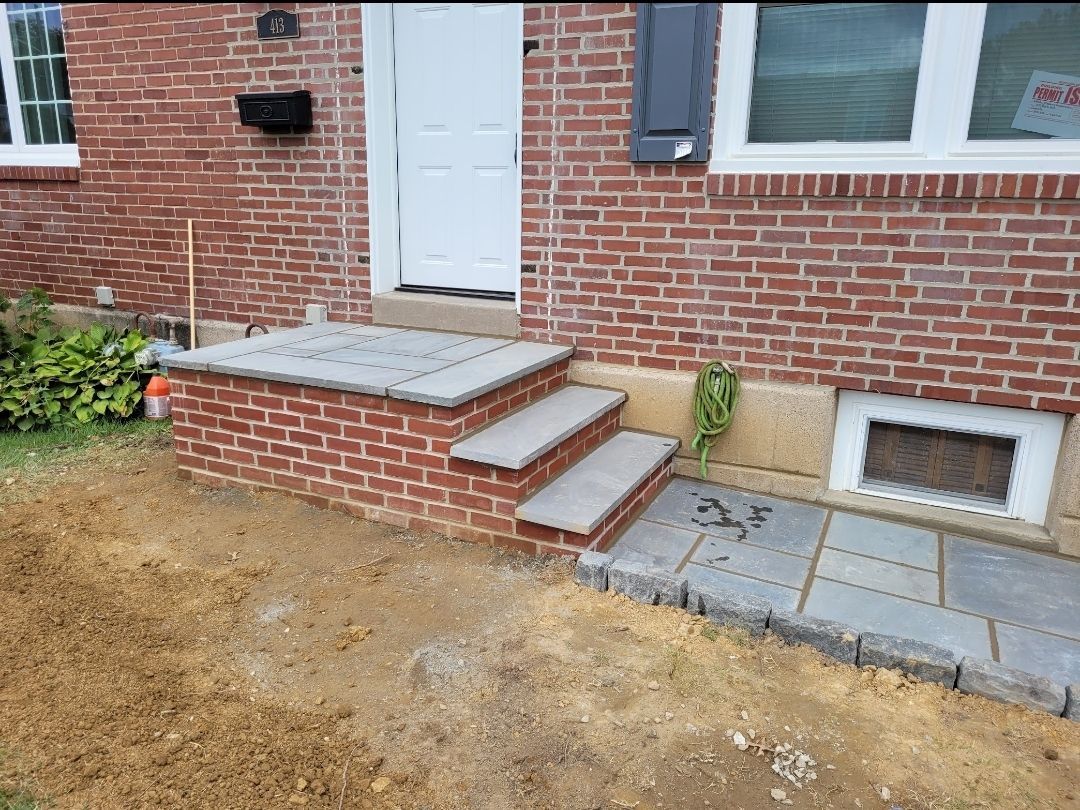 Brick home with brick steps leading to a white door; stone walkway to the right.