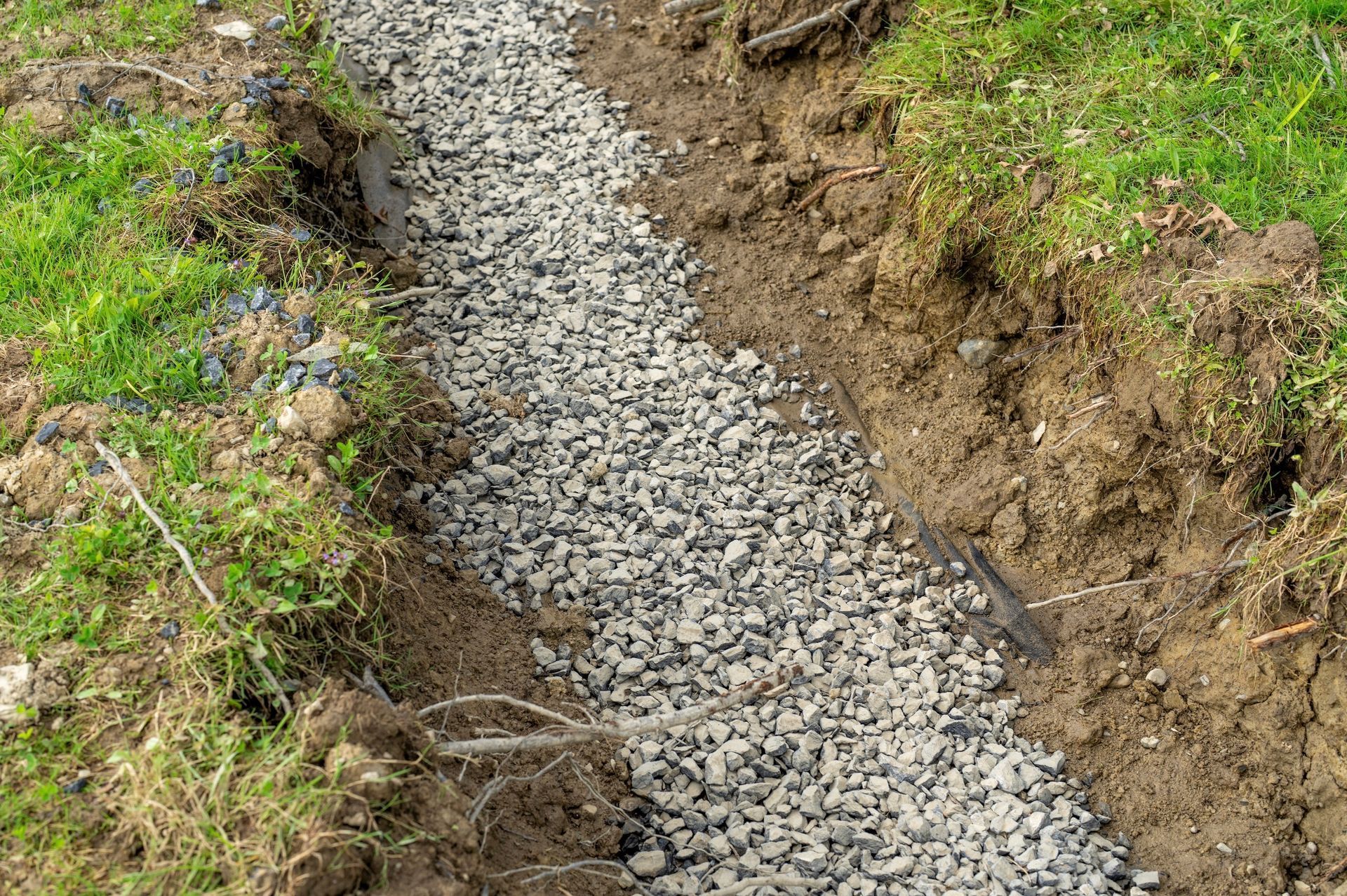 Gravel-filled trench in grassy area, likely for drainage or landscaping purposes.