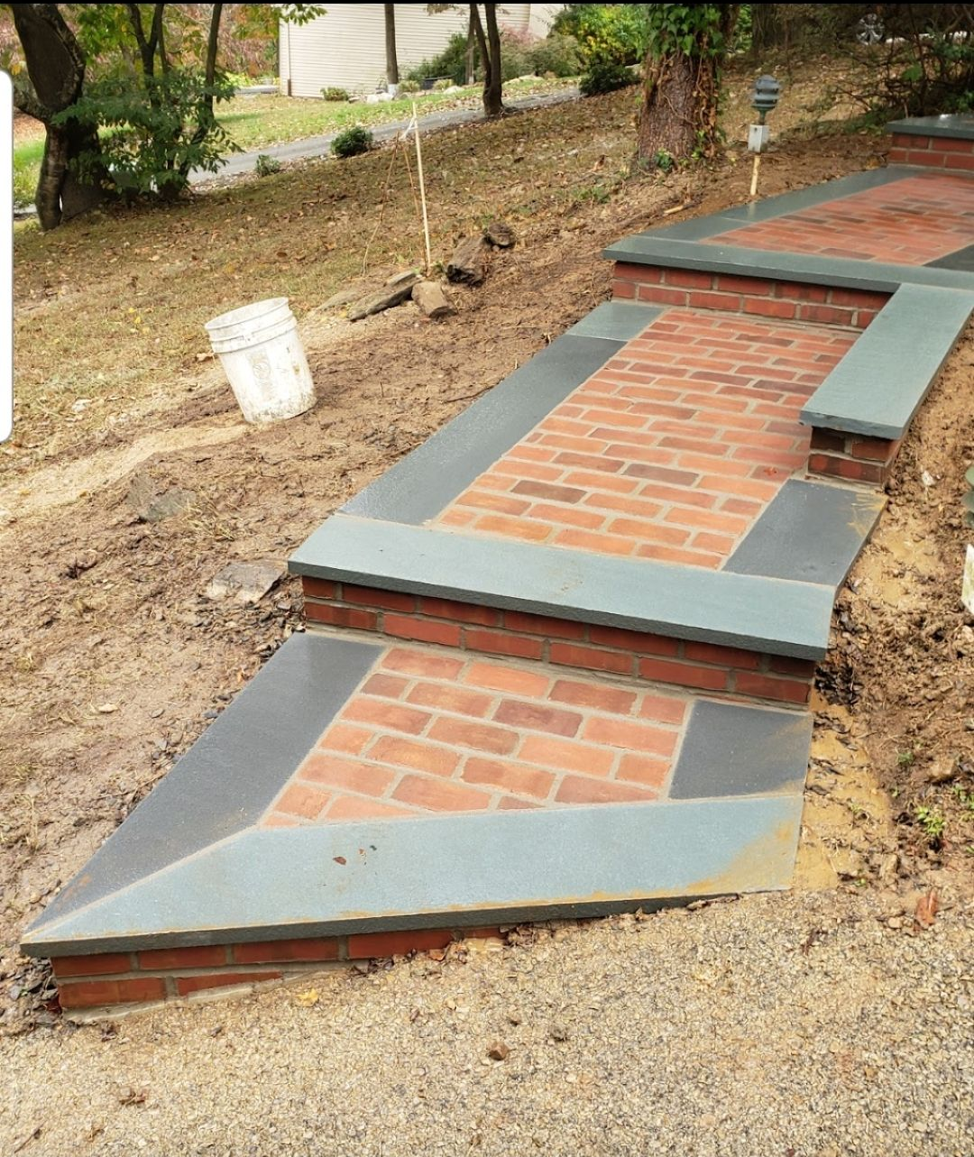 Brick pathway with gray stone borders and steps, built on a muddy hillside.