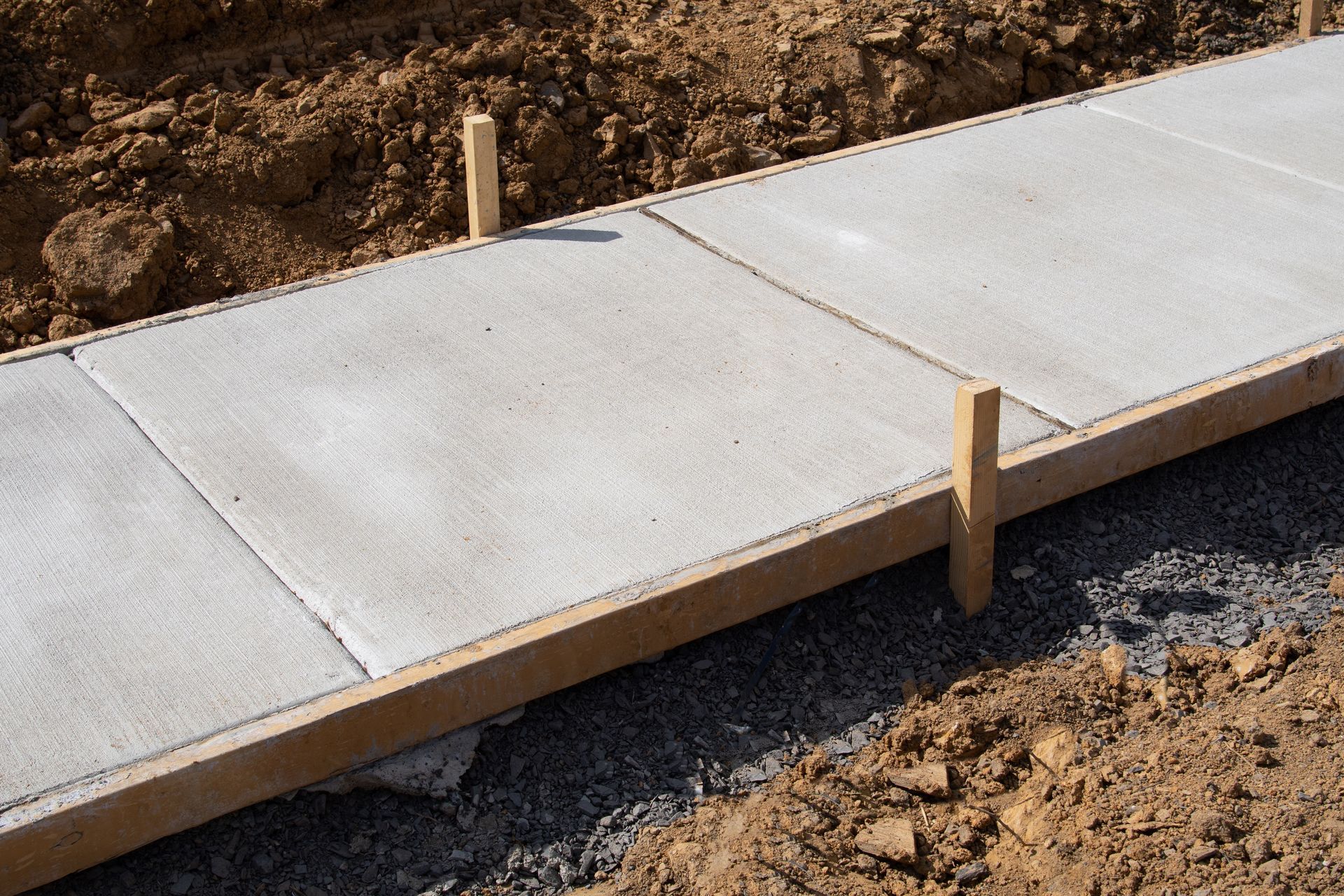 Freshly poured concrete sidewalk sections with wooden forms and stakes.