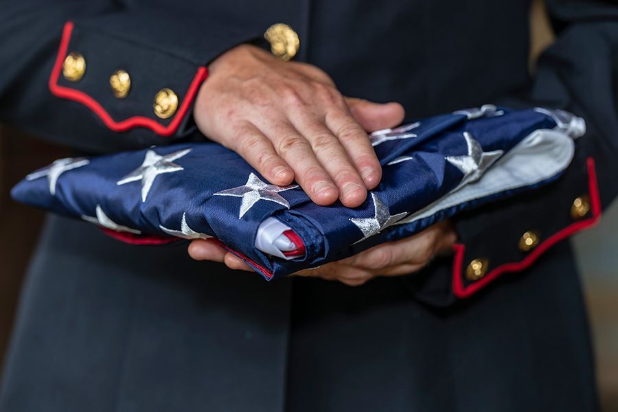 Hands in a dark uniform folding a folded American flag with white stars and red stripes.