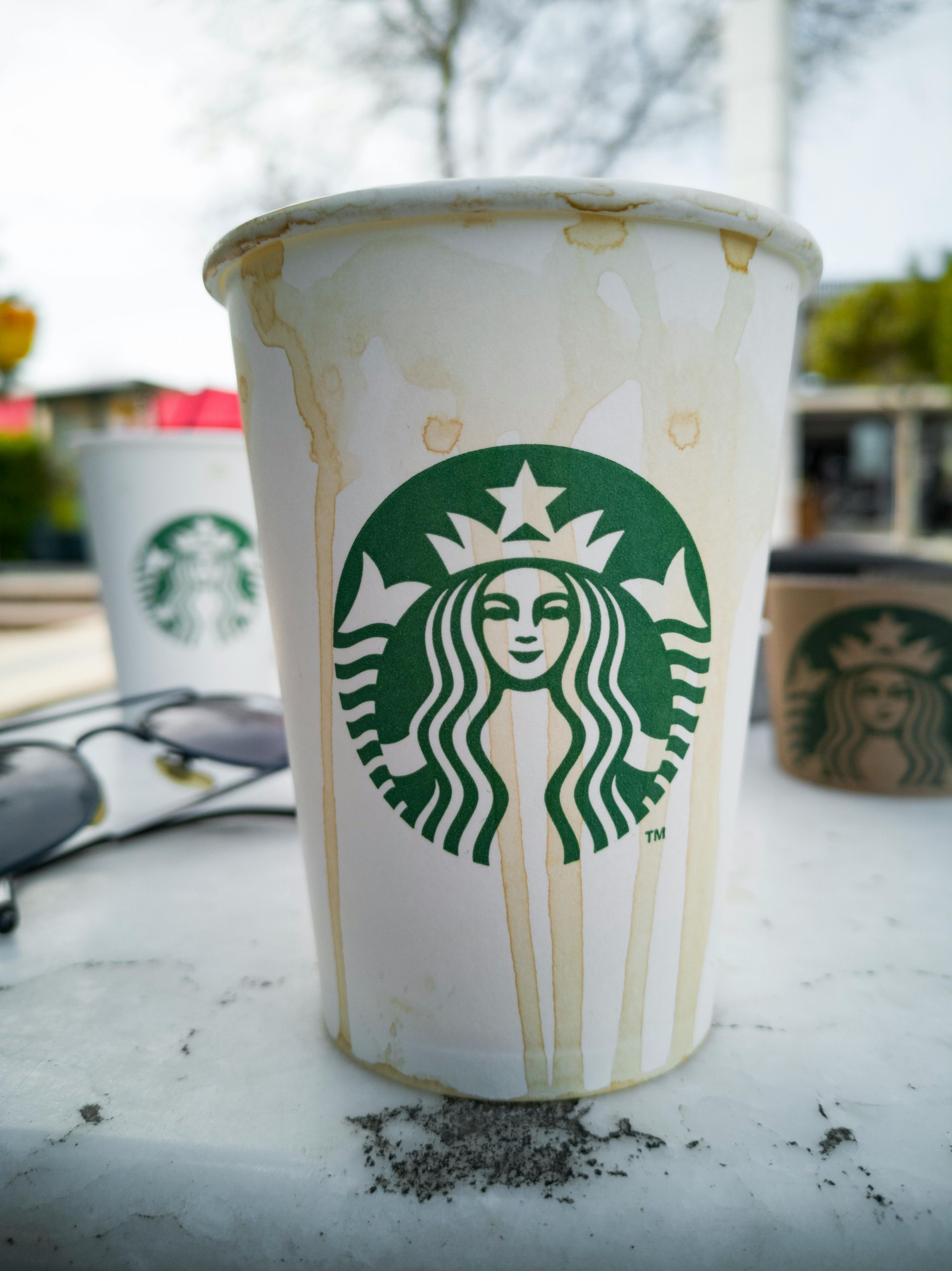 Used Starbucks paper cup with coffee stains on a white table outdoors