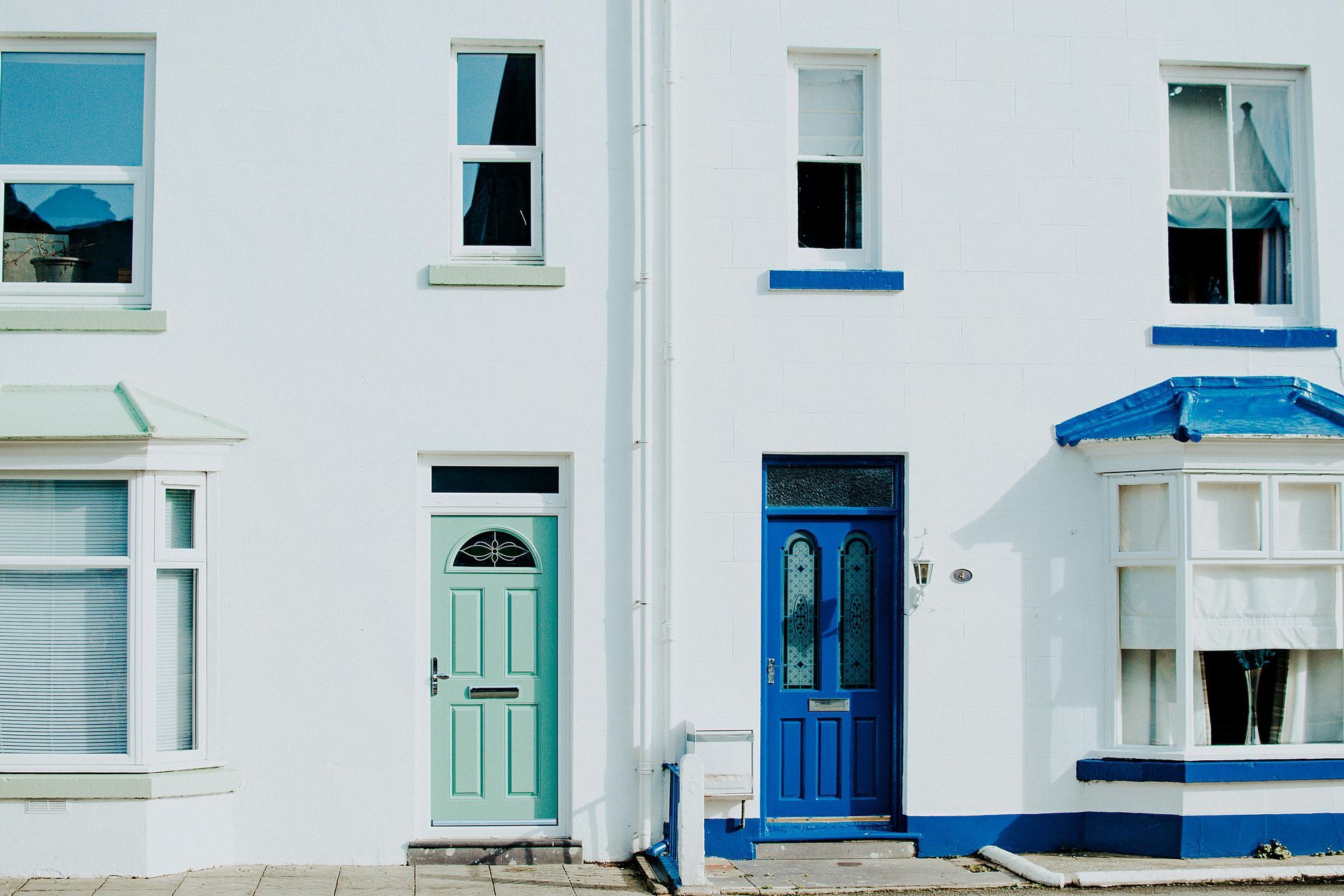 Row of white houses with colorful doors and windows, including mint green and bright blue fronts.
