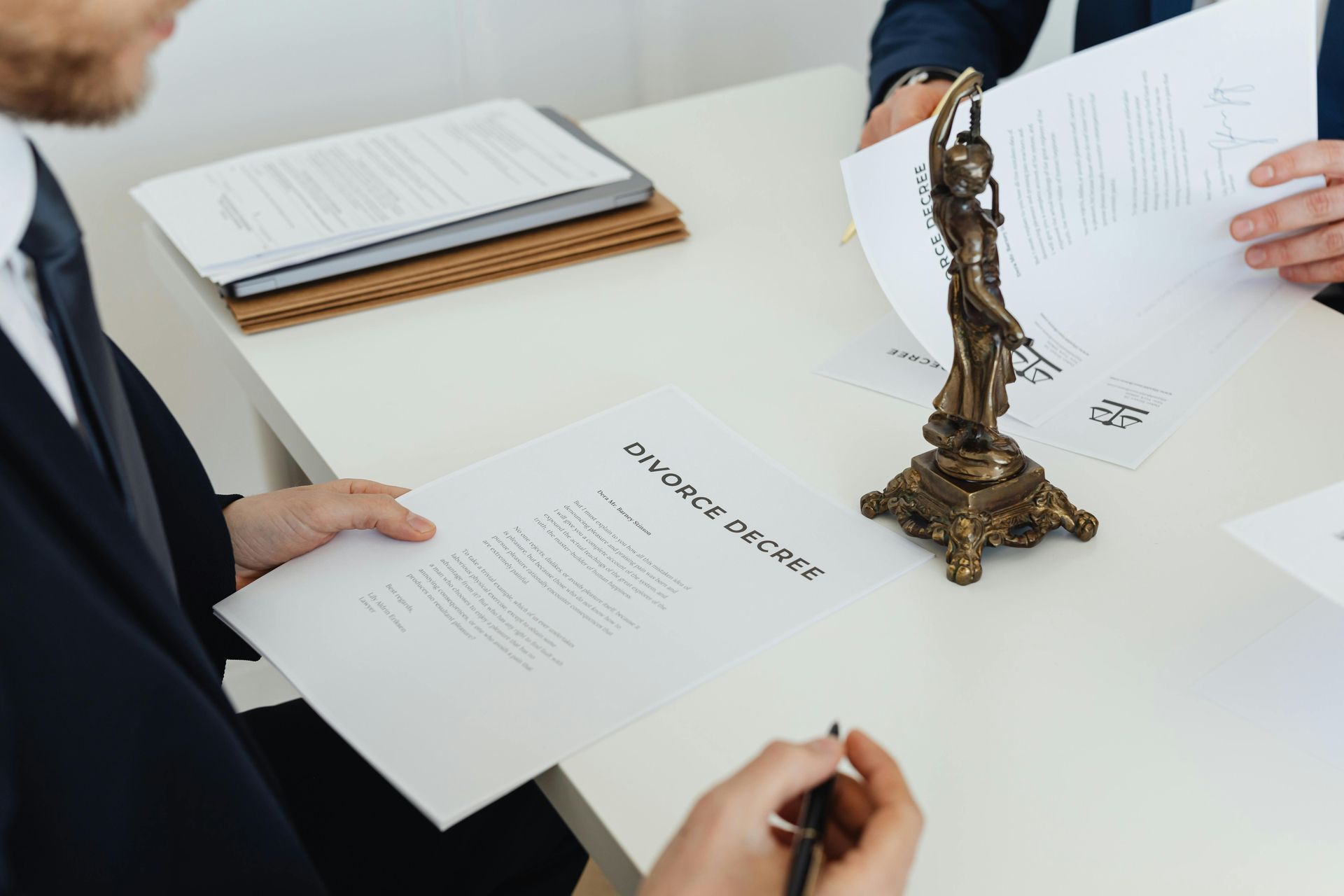 Two people review documents at a desk with a bronze figurine centerpiece on a meeting table.