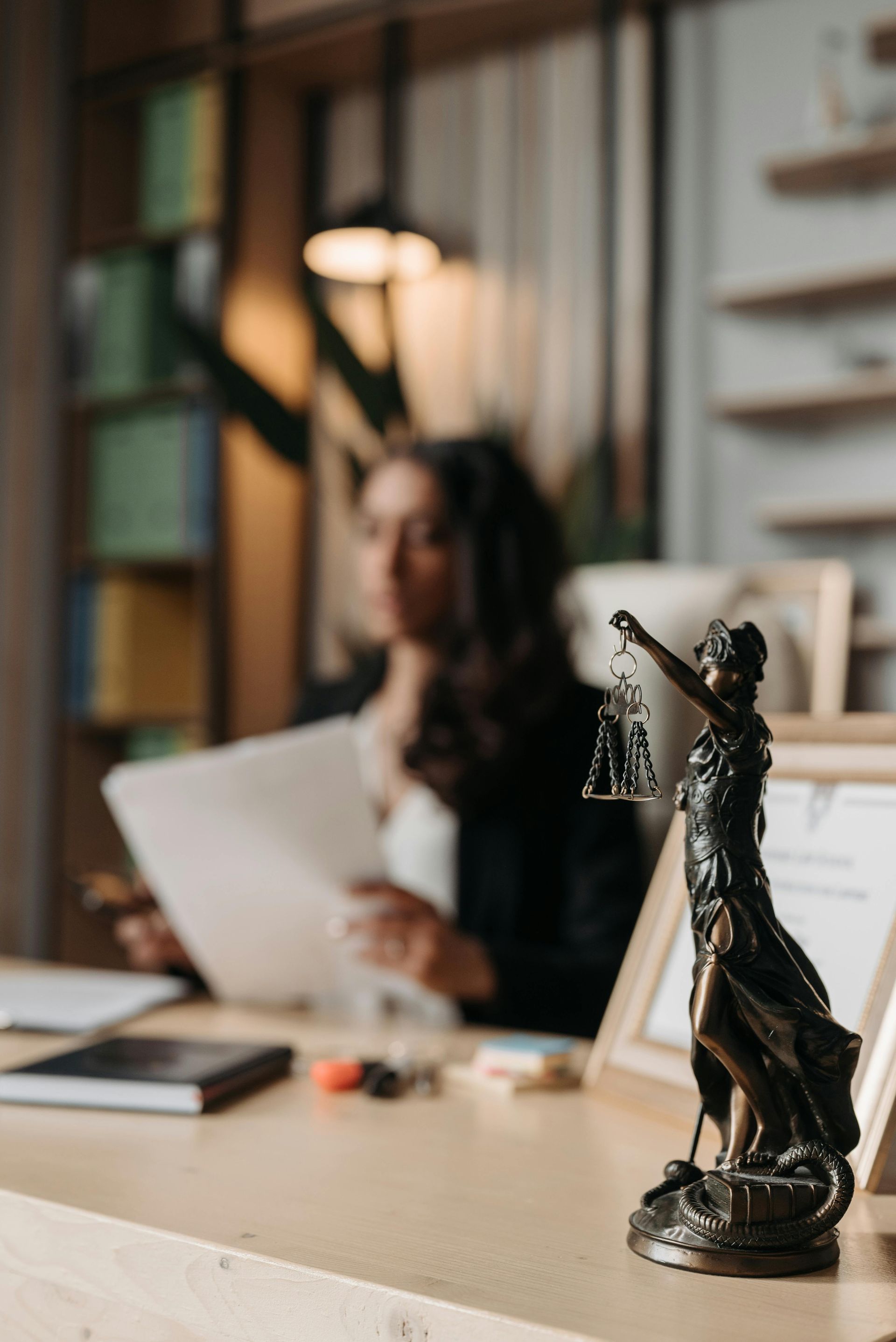 Bronze Lady Justice statue in foreground, blurred person reading papers in an office background