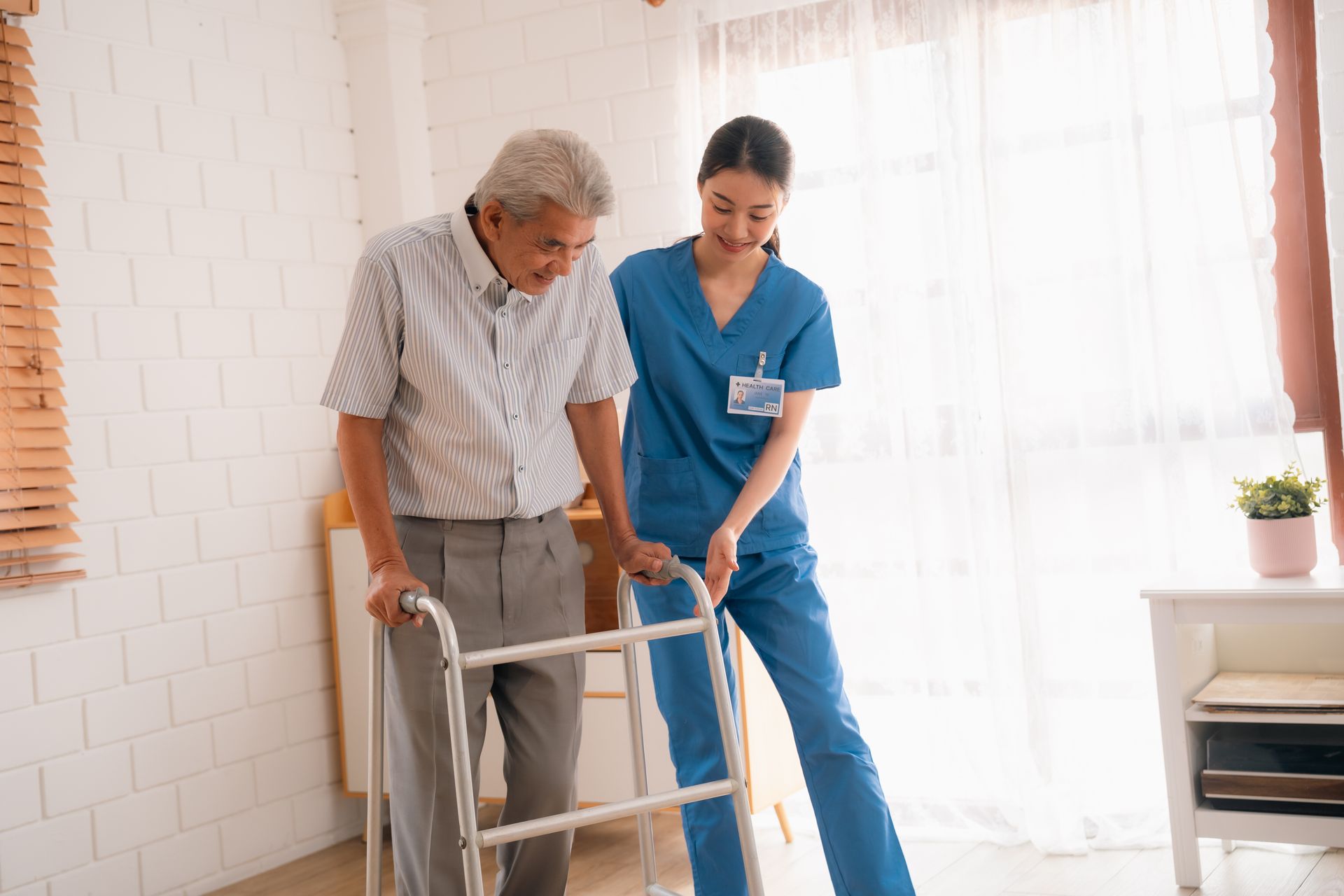 A female nurse in dark blue scrubs assists an older gentleman, inside a house. A female nurse in dark blue scrubs assists an older gentleman, inside a house.