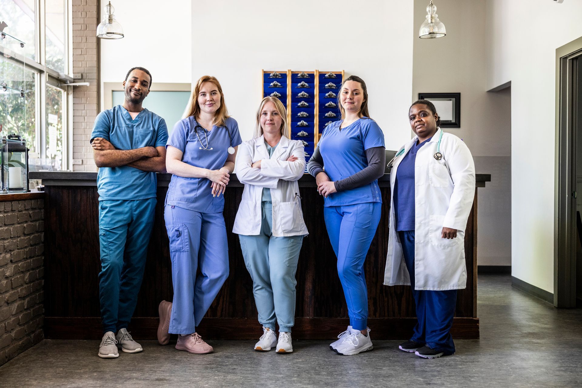 Medical staff pose in a clinic: five people in scrubs and lab coats stand behind a desk.