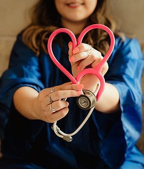 Person in blue scrubs holding a pink stethoscope shaped into a heart.
