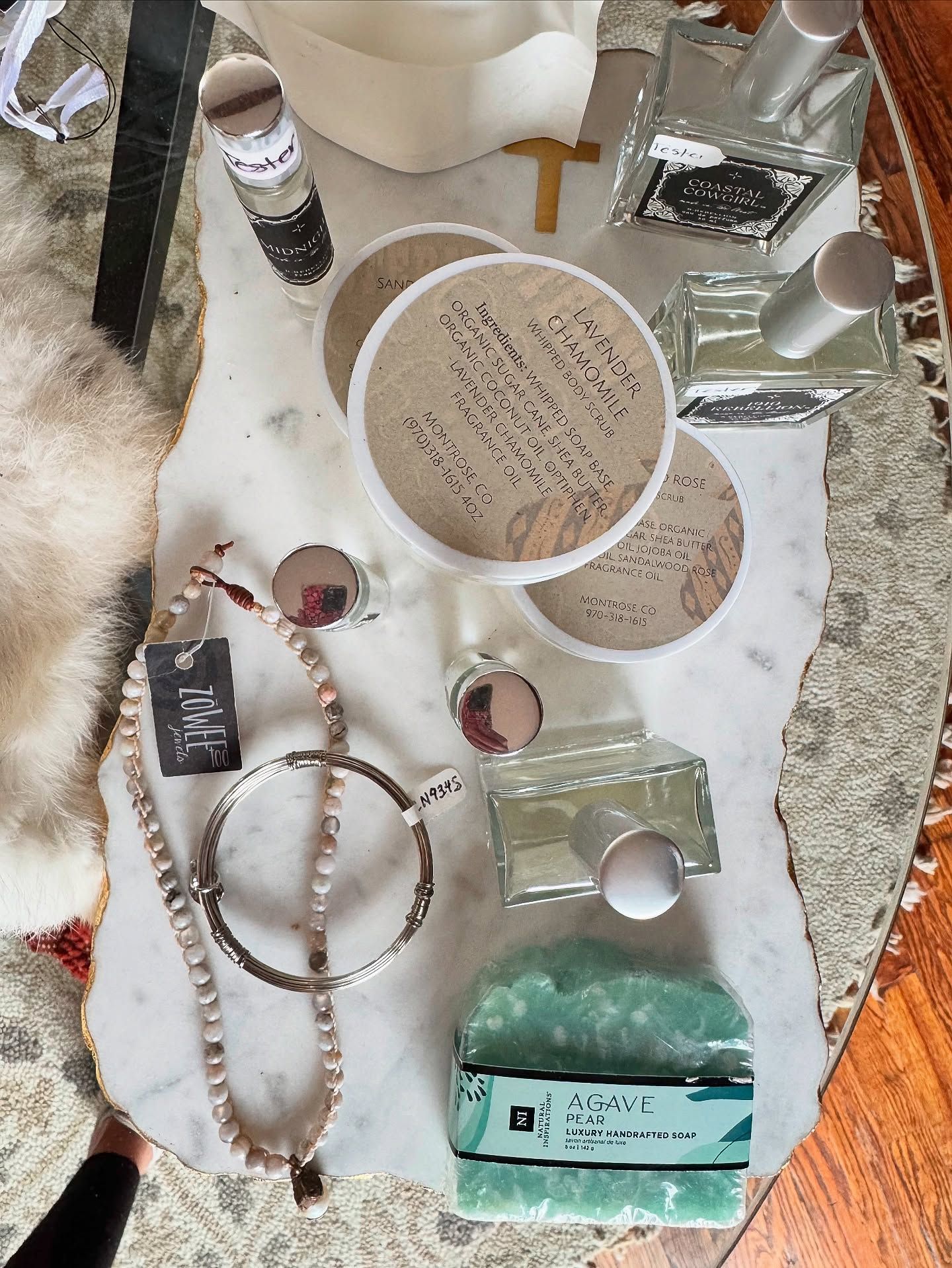Items displayed on a marble surface: jewelry, perfume bottles, coasters, glass with liquid, decorative objects.
