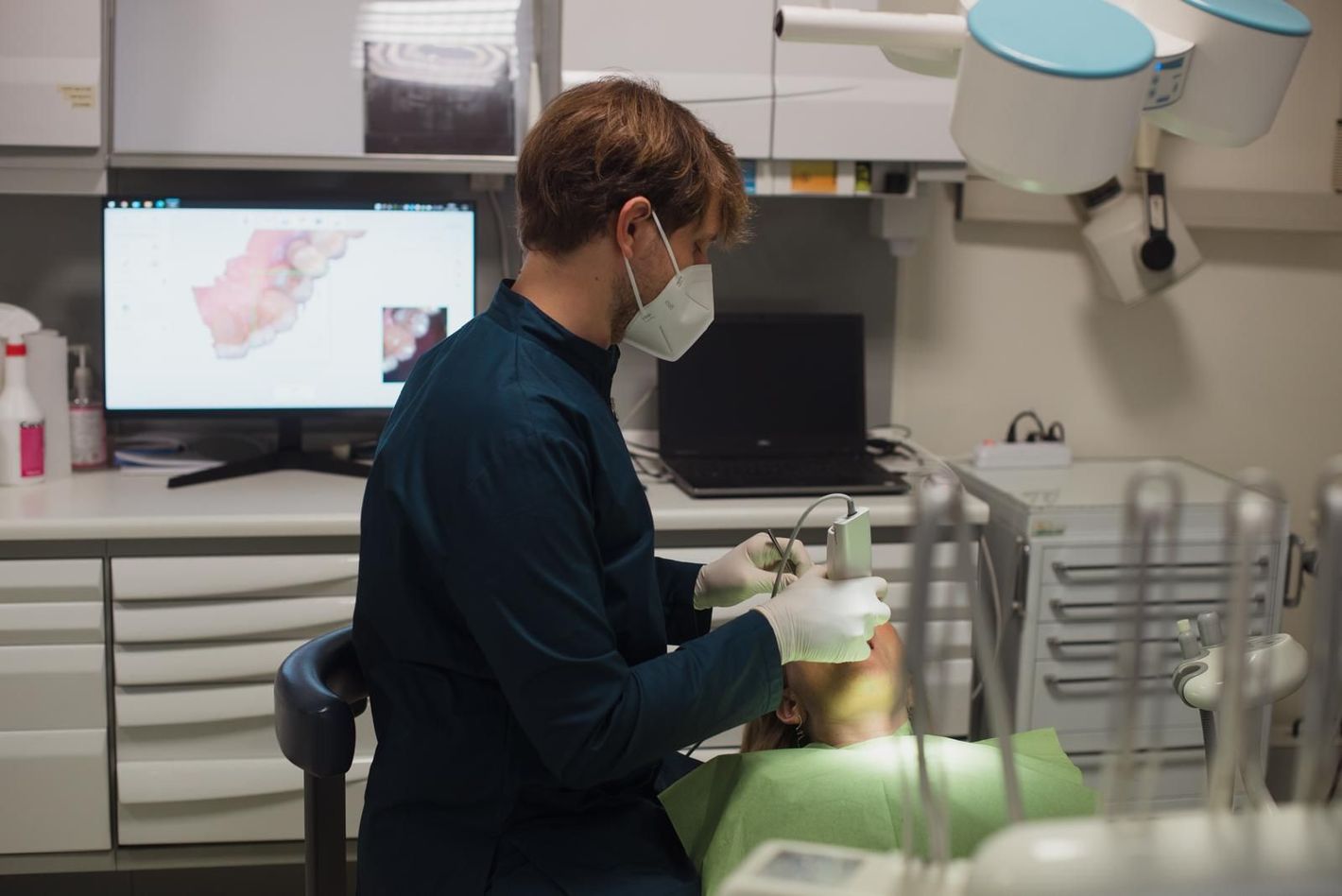 Un dentista con i guanti indica una scansione 3D di un dente su un tablet in uno studio dentistico.