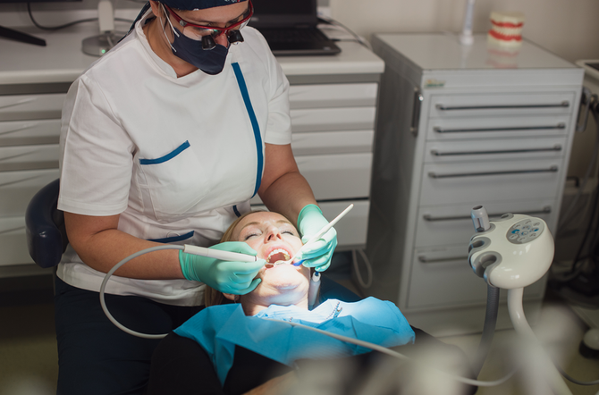 Una donna sorridente con una maglietta blu indica i suoi denti con entrambe le mani.