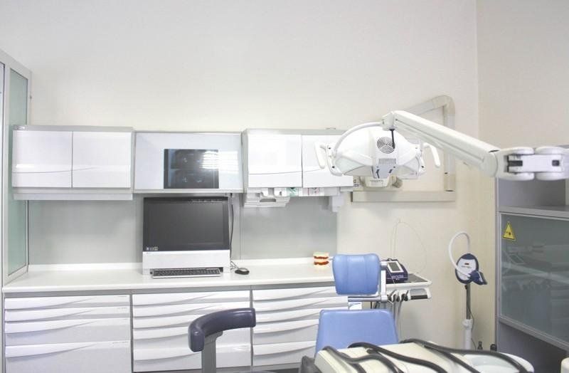 Sala visite odontoiatriche vuota con armadietti bianchi, monitor, poltrona e lampada dentale a soffitto.
