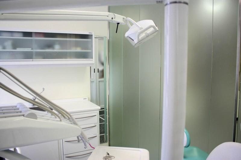 Studio dentistico con poltrona, lampada a soffitto, armadietti e pannelli a parete verdi.