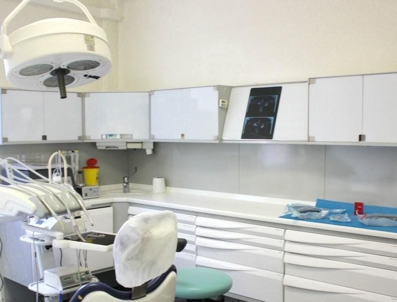 Moderna sala per trattamenti odontoiatrici con poltrona, lampada a soffitto, armadietti e attrezzature.