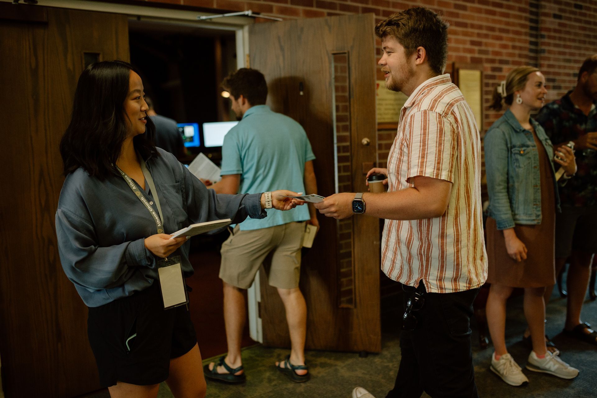 Photo of people walking into the sanctuary on a Sunday morning, being greeted and handed a worship folder.