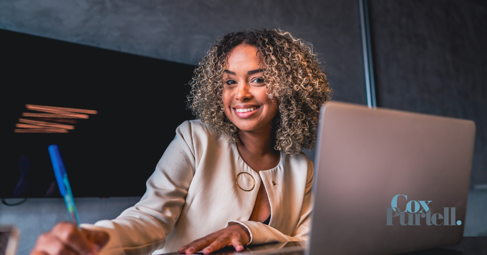 Smiling person at a desk using a laptop in a modern office setting