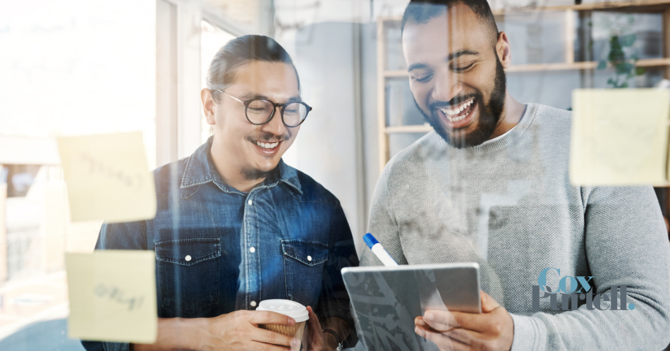 two men smiling looking at an iPad