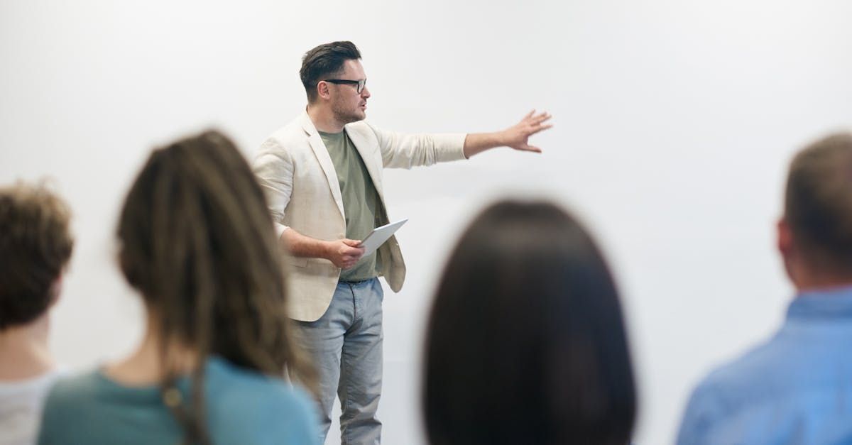 Photo of a man pointing at a white wall with people watching