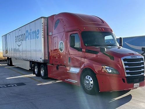 A red semi truck with a white trailer is parked in a parking lot.