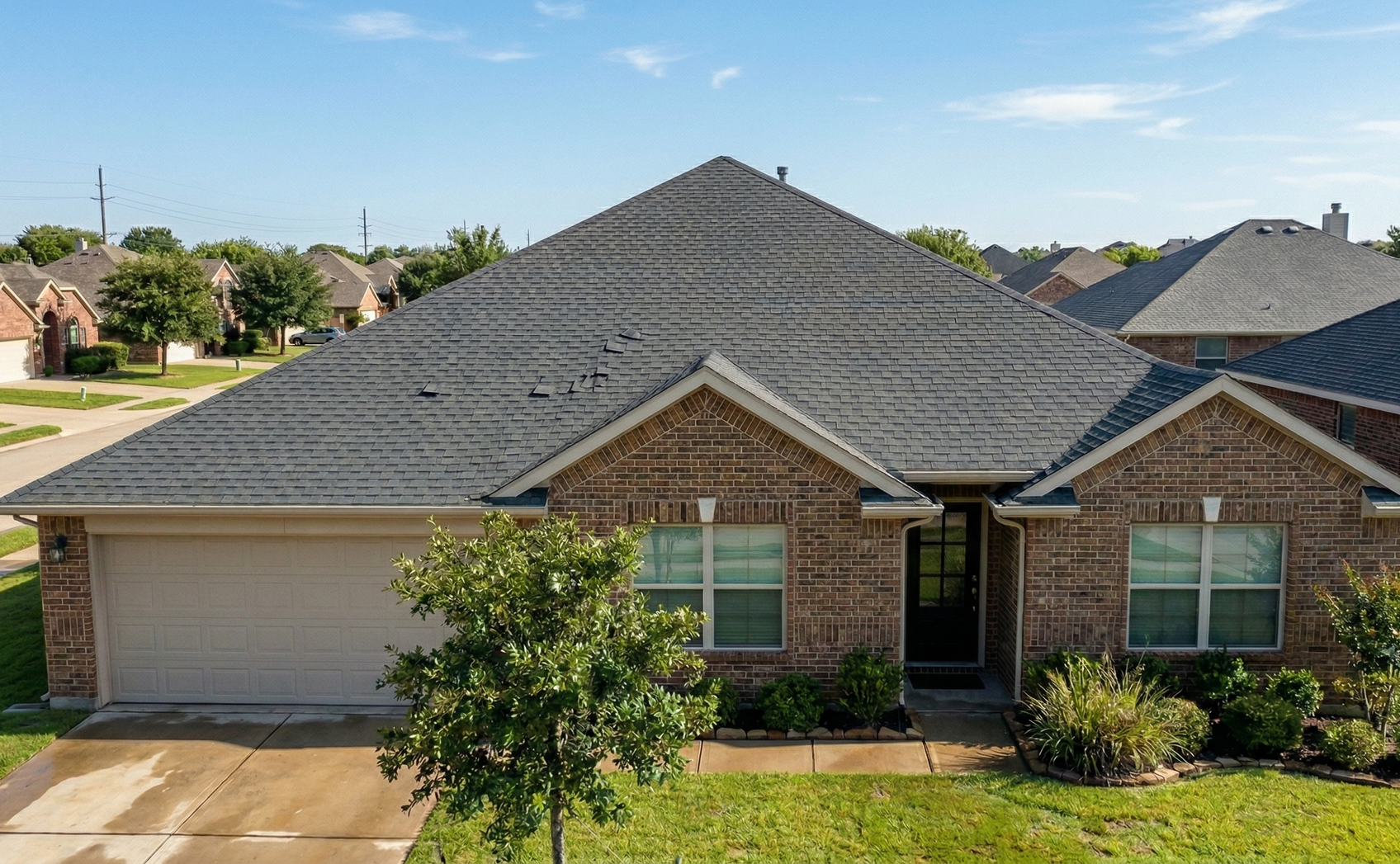 A single-story brick house with a dark shingled roof, two front-facing gables, and an attached two-car garage.