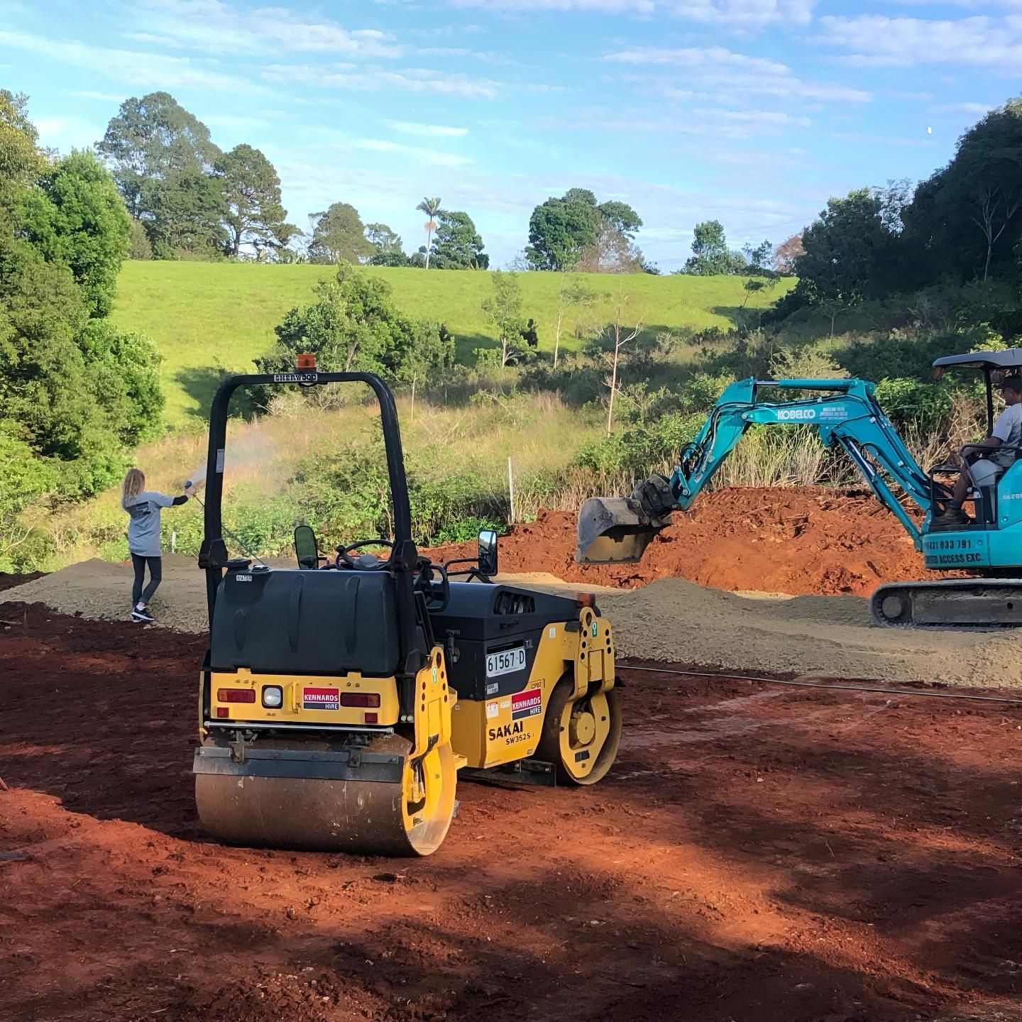 A Yellow Roller is Sitting on Top of a Dirt Field Next to a Blue Excavator — Limited Access Excavation In Alstonville, NSW