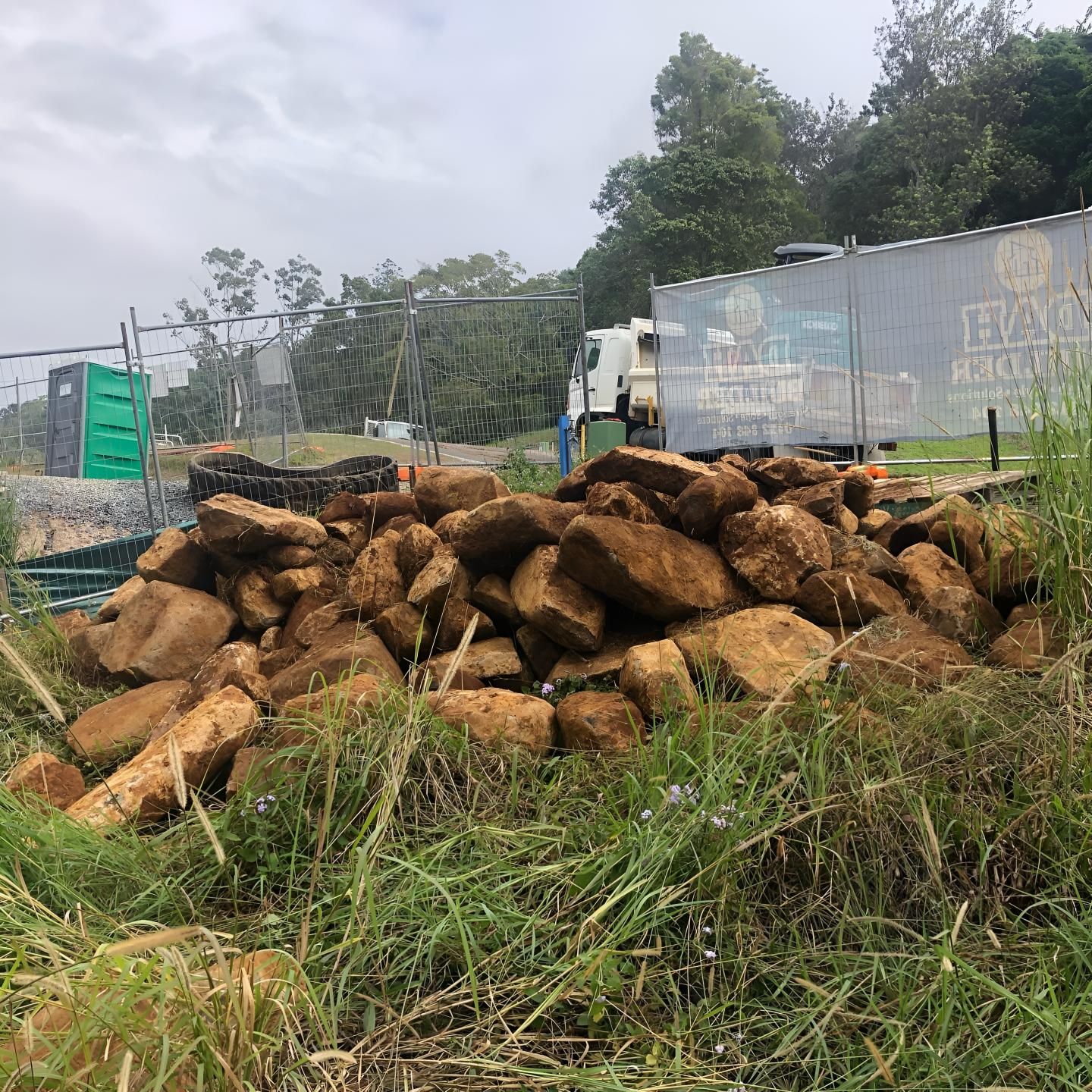 A Pile of Rocks is Sitting in the Grass Next to a Truck — Limited Access Excavation In Lismore, NSW