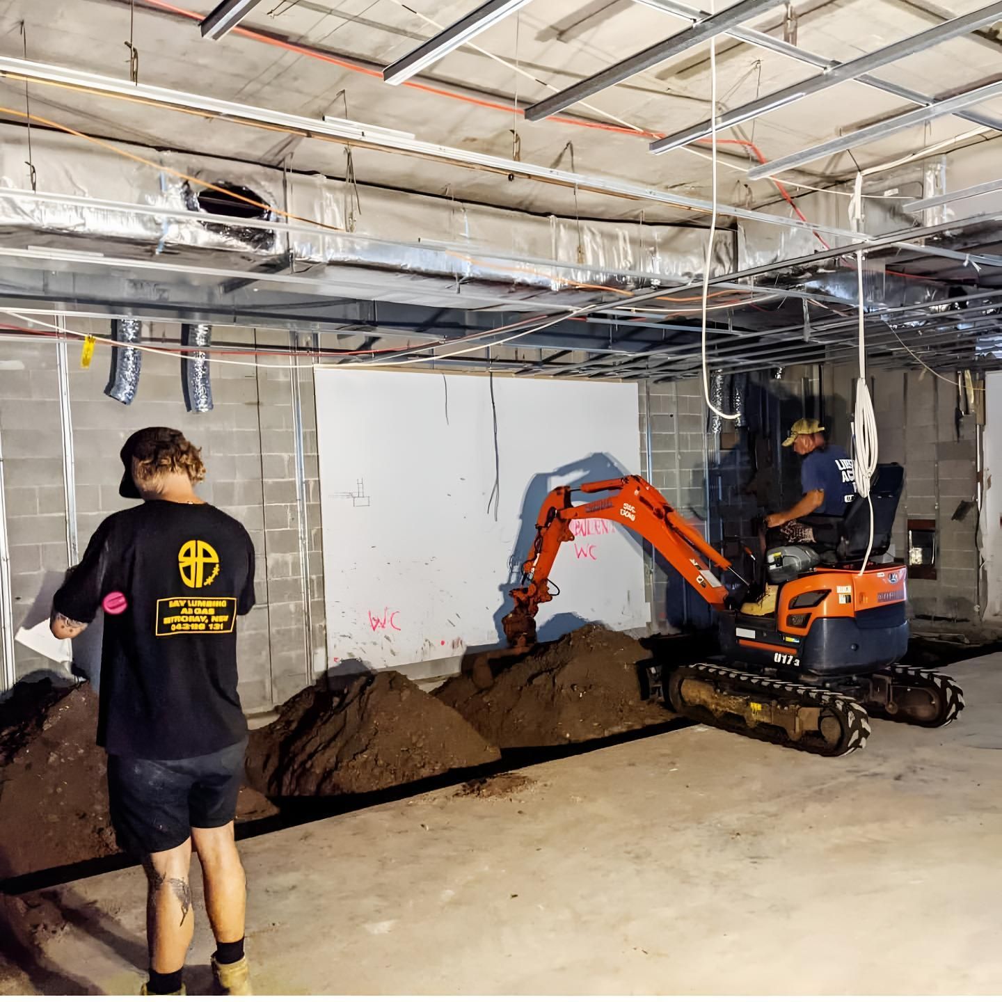 A Man is Standing Next to a Small Excavator in a Basement — Limited Access Excavation In Yamba, NSW