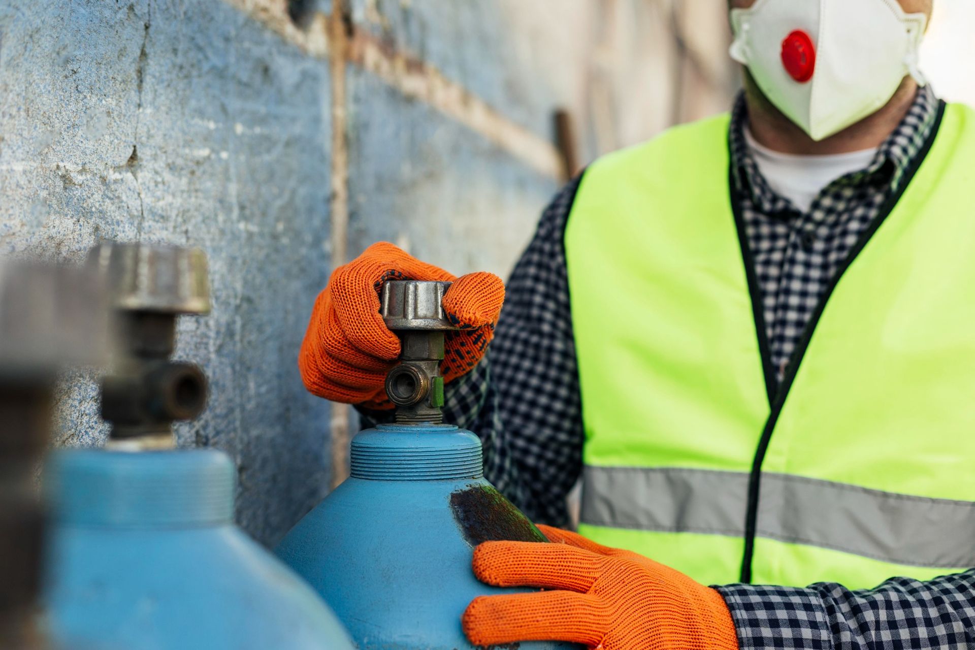 Una persona con equipo de seguridad abre una válvula en un cilindro de gas azul.