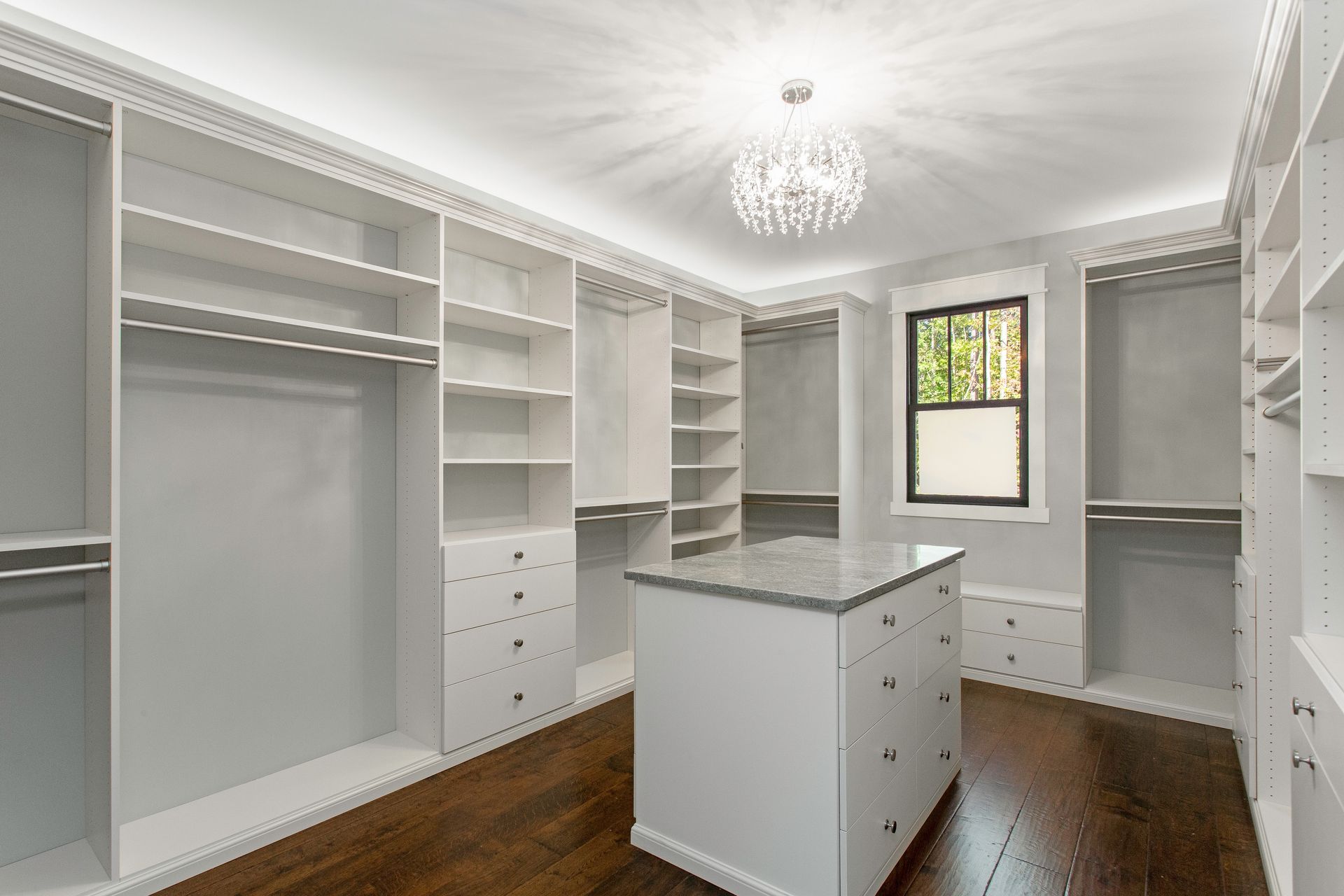 Bright custom walk-in closet with white shelving, drawers, and central island on dark wood floors