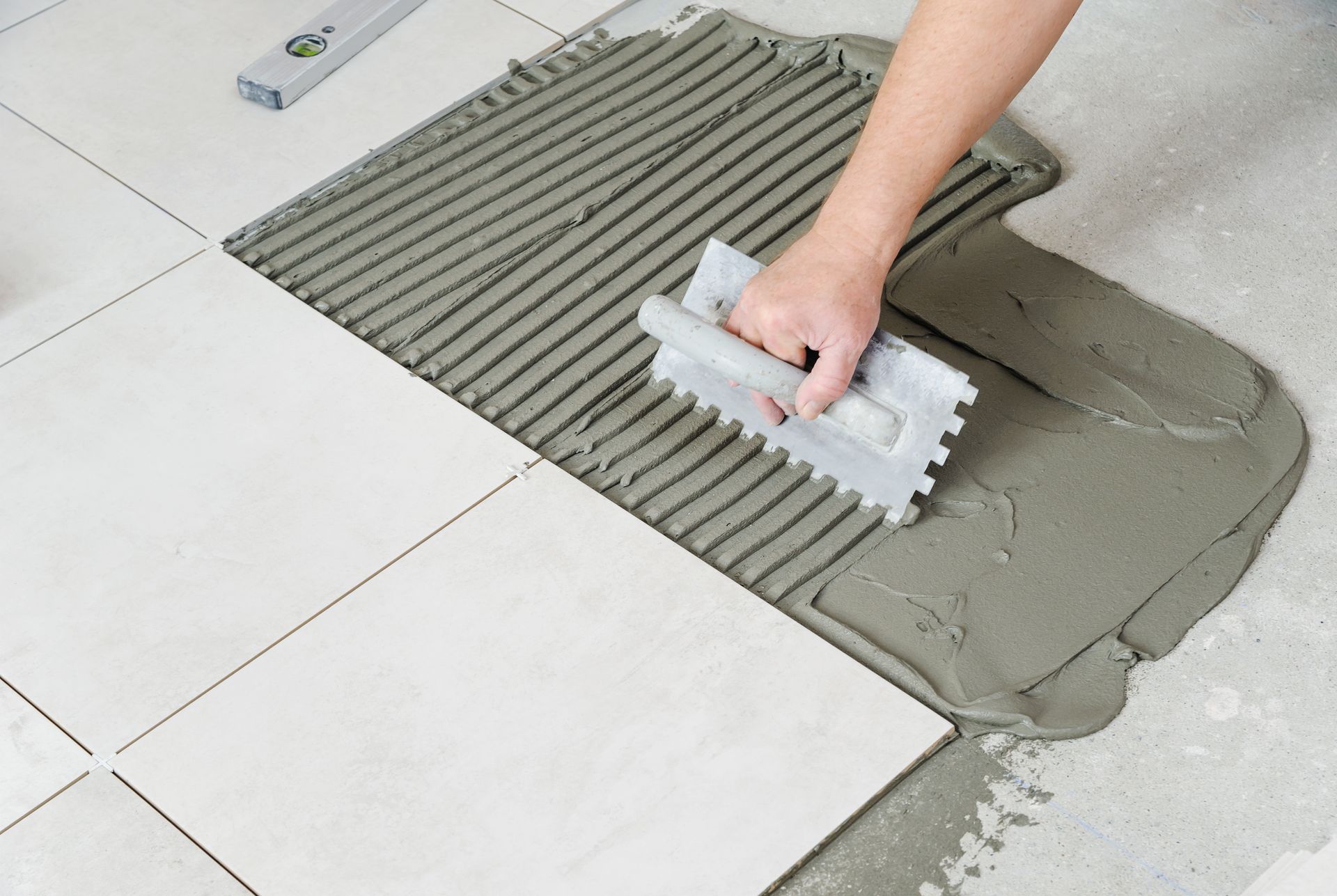 Hand spreading gray tile adhesive with a notched trowel on a tiled floor