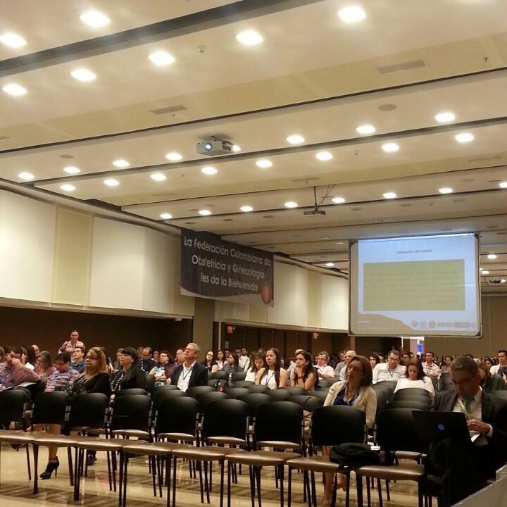 El público de la conferencia está sentado en un aula, frente a una pantalla donde se proyecta una presentación.