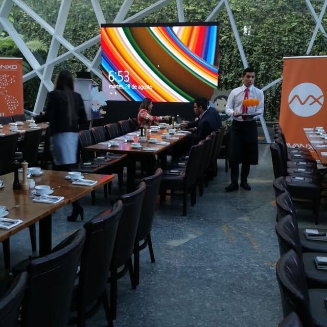 Comedor al aire libre con una gran pantalla colorida y personal preparando las mesas al atardecer.
