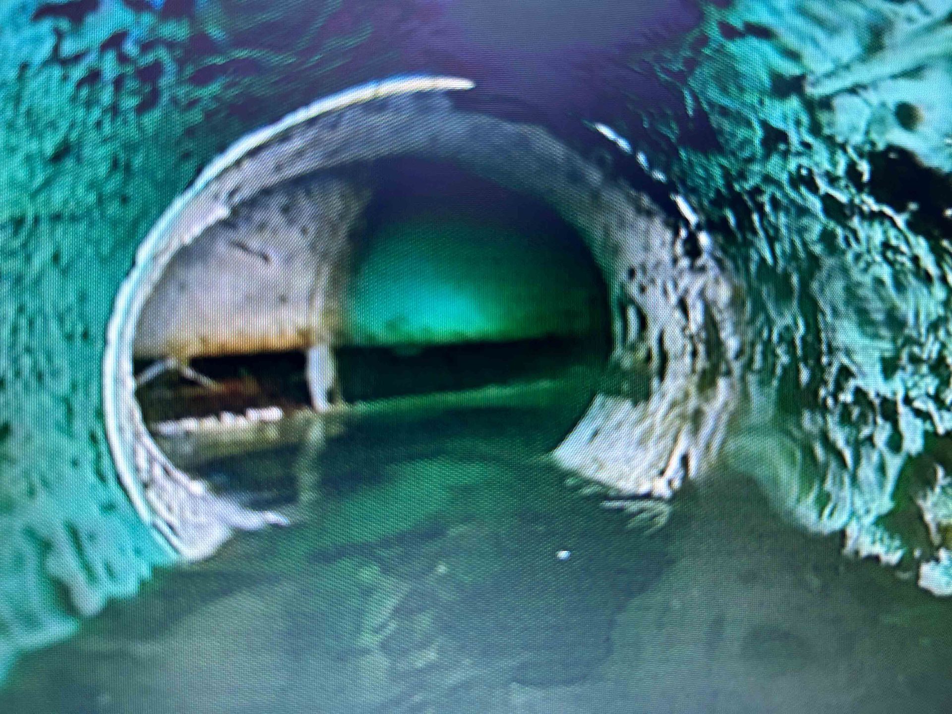 Intérieur d'un tuyau de drainage en béton turquoise avec de l'eau qui coule et une petite ouverture devant